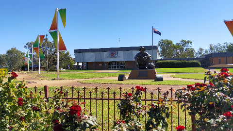 Bronze soldier statue in garden with flags and modern building.