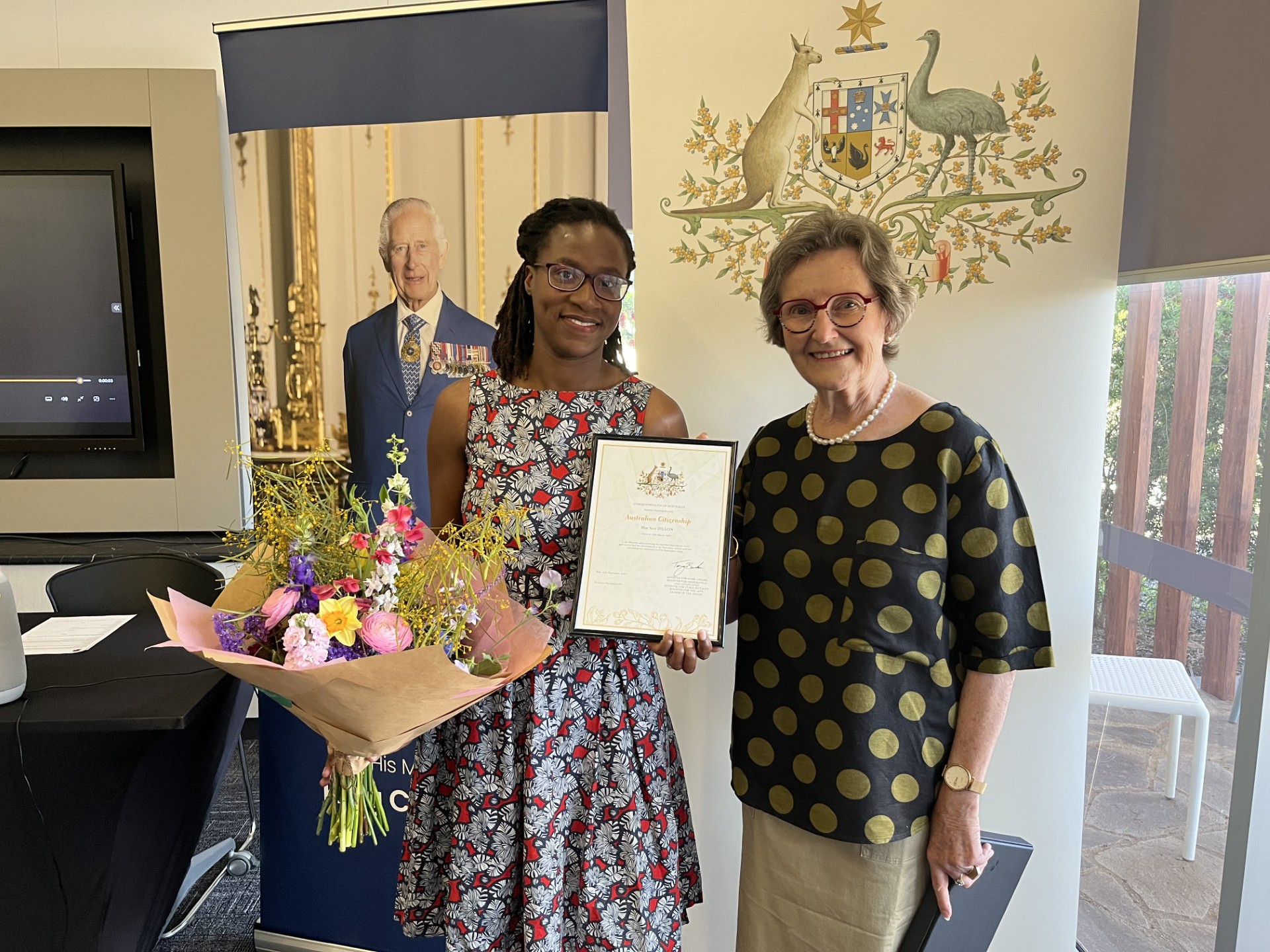 Dark lady holding flowers and certificate with another lady smiling at camera